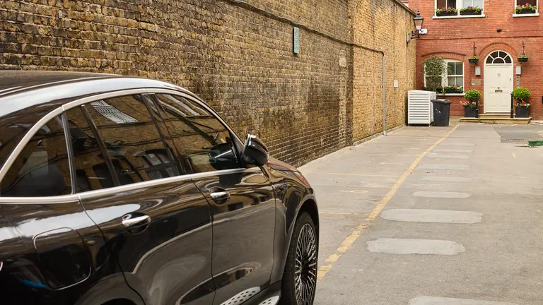 A black car parked alongside a brick wall 