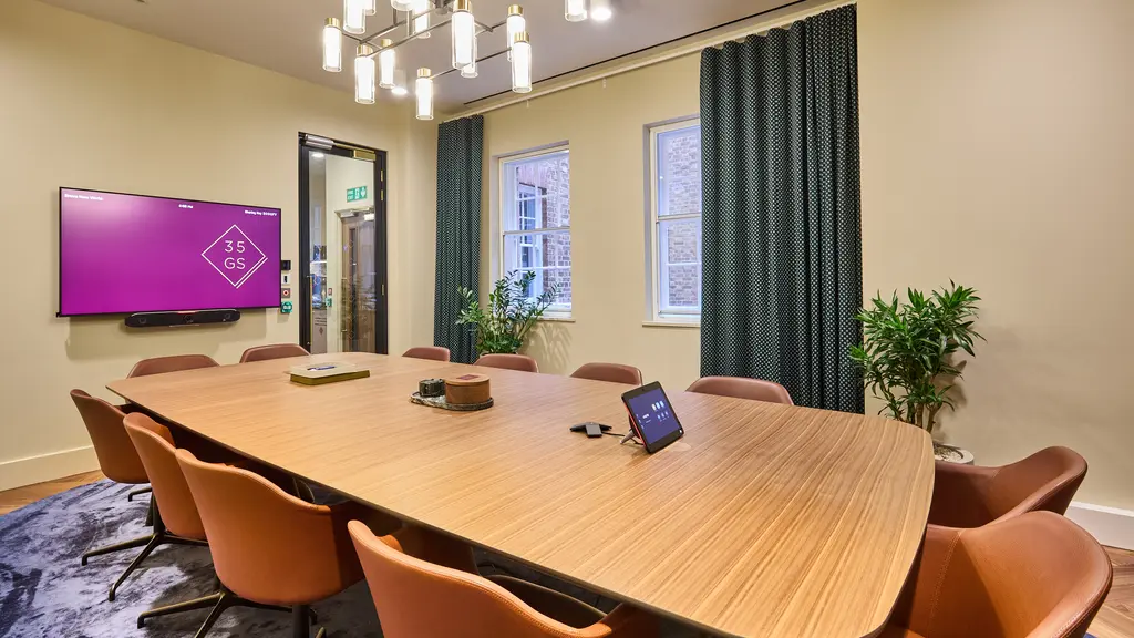 Meeting room with a big table with chairs around it facing a screen