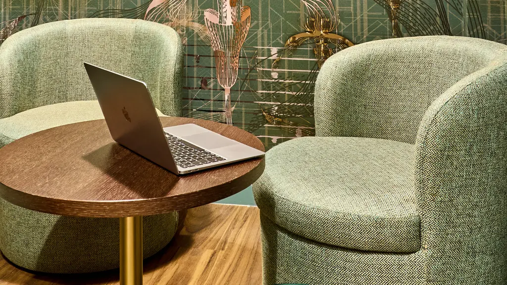 A meeting room with two green chairs and a laptop on a small circular table