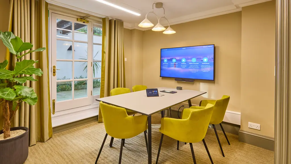 A meeting room with five yellow chairs, a table and a TV screen