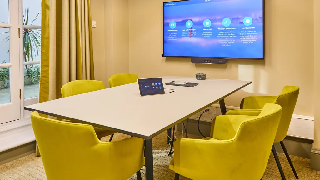 A meeting room with five yellow chairs and a TV screen