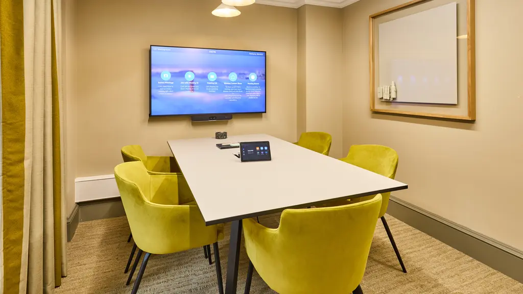 A meeting room with five yellow chairs and a TV screen