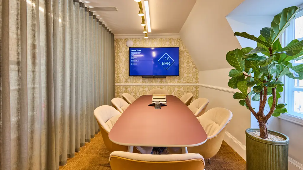 A meeting room with a pink table, a TV screen and a yellow carpet