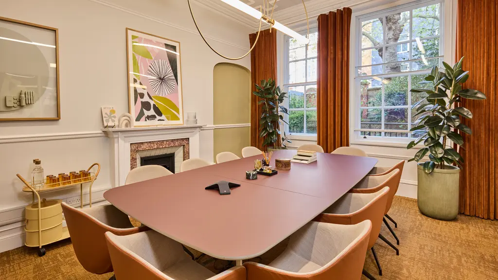 A meeting room with a long pink table surrounded by chairs and with artwork on the walls
