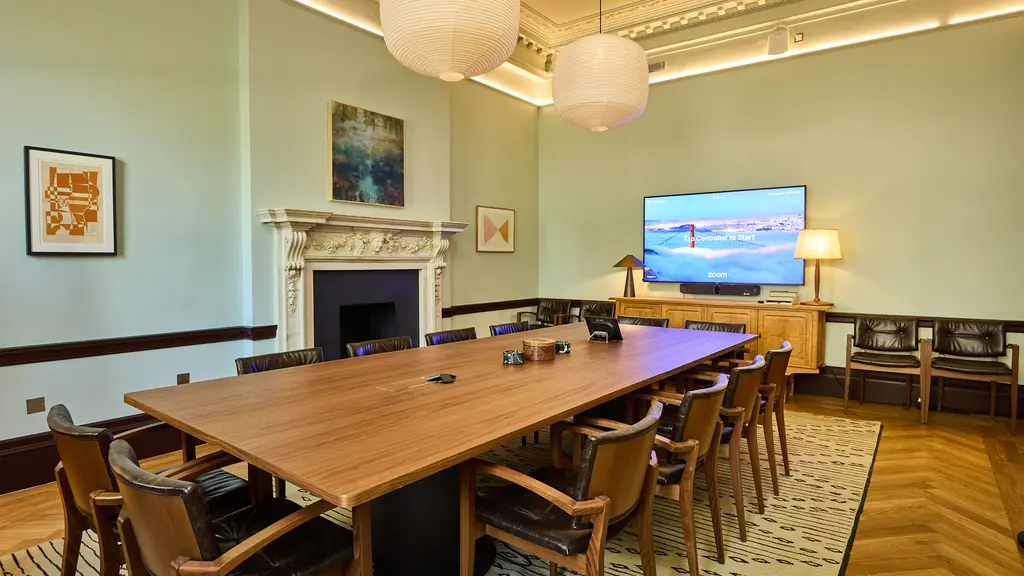 A boardroom style meeting room with a long table, chairs and TV screen