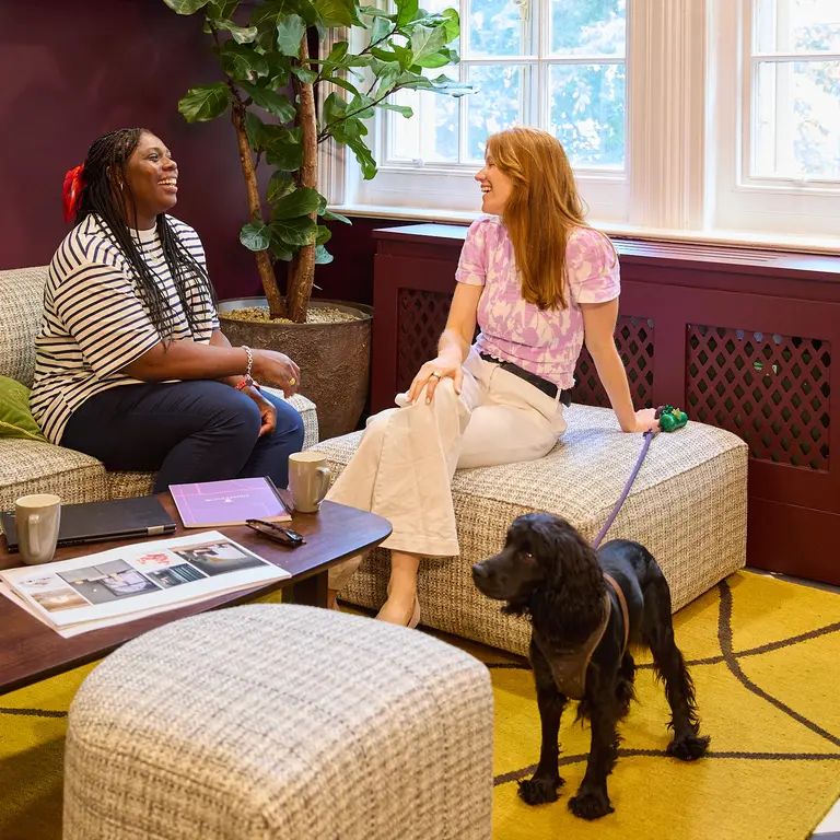 Two women talking on a sofa with a dog