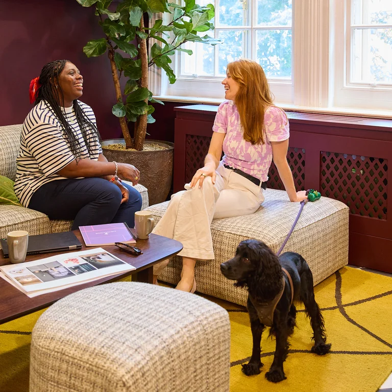 Two women talking on a sofa with a dog