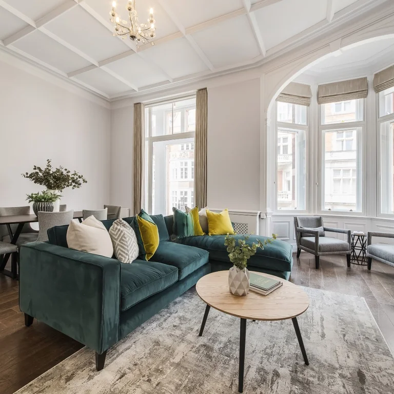 A living room with a green corner sofa and large windows
