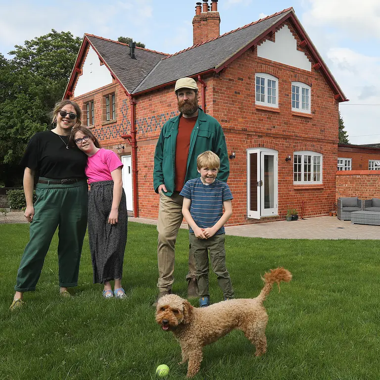 A family of four and a dog standing in a garden with a house in the background