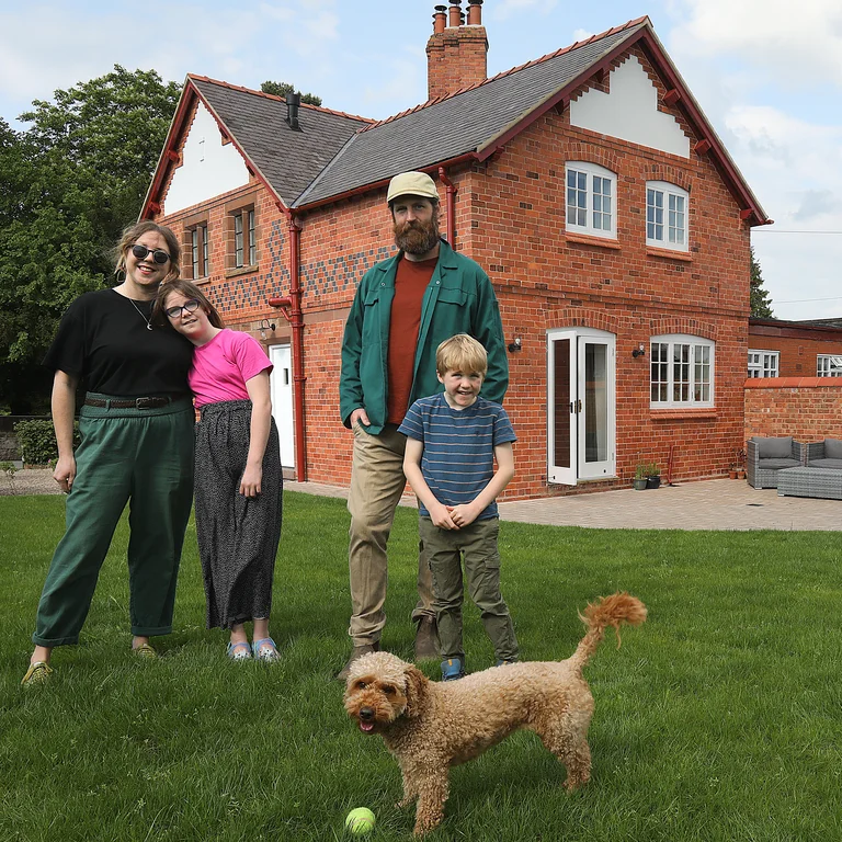 A family of four and a dog standing in a garden with a house in the background