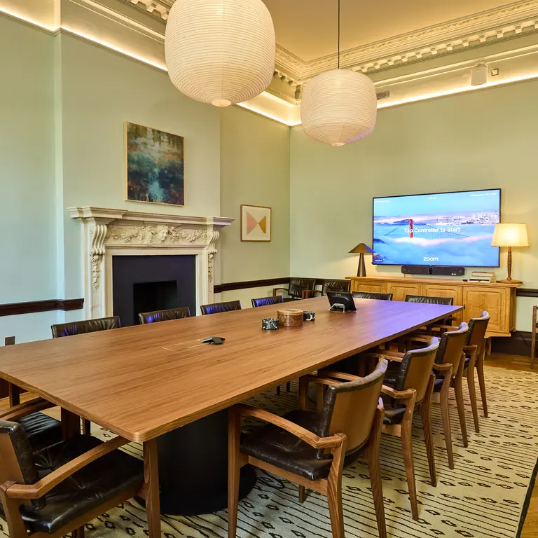 A boardroom style meeting room with a long table, chairs and TV screen